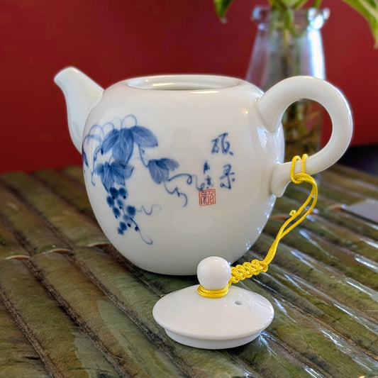 White porcelain teapot with the lid removed, with blue painted leaf design and Chinese characters.