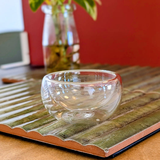 Double walled small glass cup on a green mat against a terra cotta background.