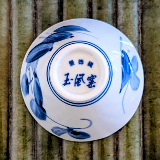 Bottom of a white porcelain tea cup painted with blue leaf design and Chinese characters on a green mat.