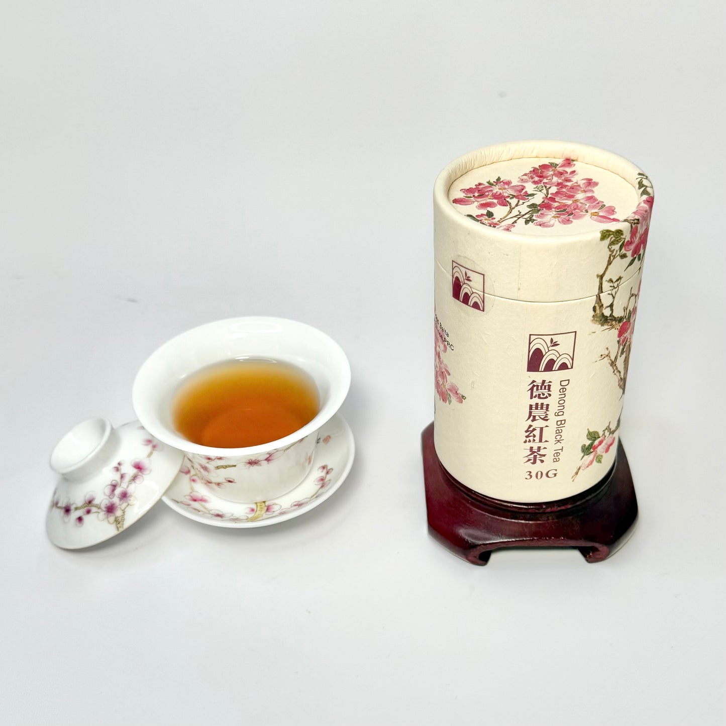 Tea canister with floral design next to a teacup filled with tea on a white background