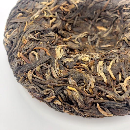 Close-up of a compressed tea cake with dried tea leaves on a white background