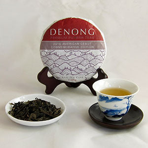 Denong tea cake with a cup of tea and loose tea leaves on a white background