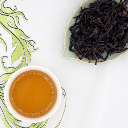 Tea leaves and cup of brewed tea. The leaves are dark brown and auburn, long and wiry.  Brewed tea is amber.