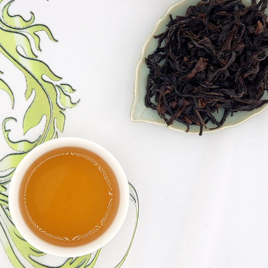 Tea leaves and cup of brewed tea. The leaves are dark brown and auburn, long and wiry.  Brewed tea is amber.
