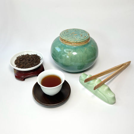 Tea set with a green ceramic jar, white cup, and wooden tongs on a white background