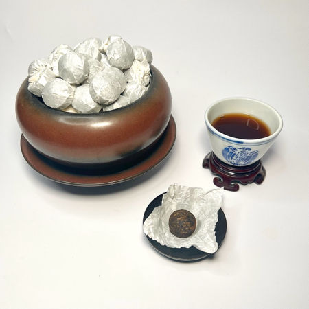Single serving compressed pu-erh tea, wrapped in tissue paper, next to a cup of brewed tea.