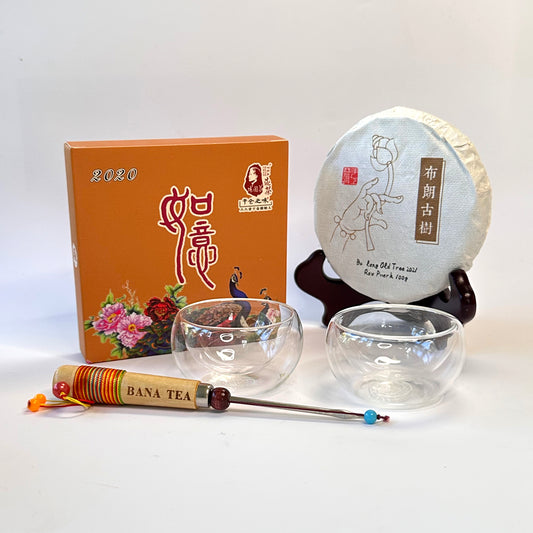 Tea packaging with a tea cake, two glass cups, and a tea pick tool on a white background