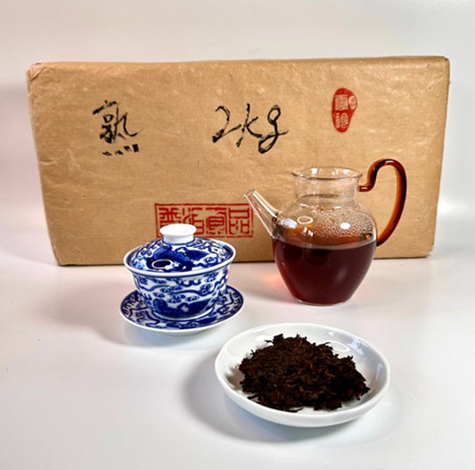 Tea set with a teapot, blue and white teacup, and bowl of tea leaves in front of a cardboard box.
