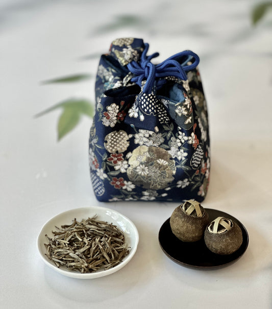 Floral fabric drawstring bag with a bowl of tea leaves and two tea balls on a light background