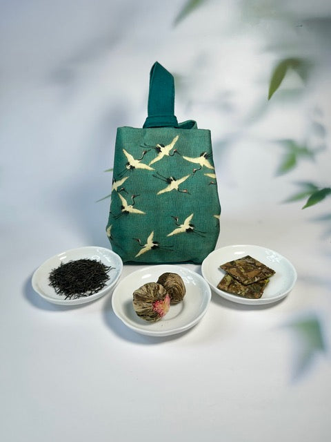 Cloth pouch with bird design on a white surface with tea leaves and tea packages.