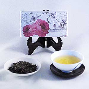 Tea leaves in a bowl, brewed tea in a cup, and a tea brick packaged with floral design on a white background