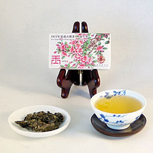 Tea leaves and a cup of tea on a white surface with a packaged tea cake in the background.