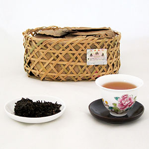 Tea leaves in a woven basket, a cup of tea with a floral design, and loose tea on a white background.