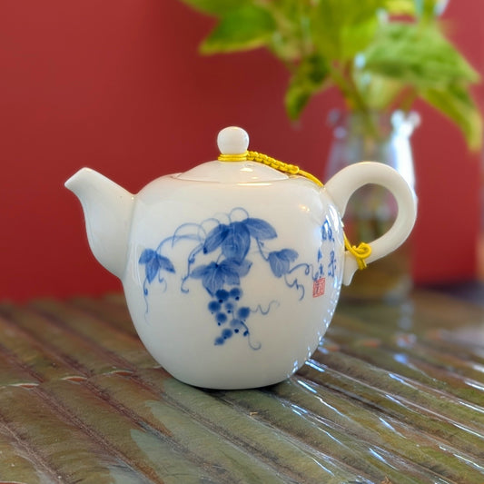 Porcelain white tea pot with blue hand painted design of leaves and flowers on a terracotta background.
