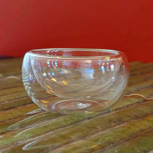 Double walled small glass cup on a green mat against a terra cotta background.