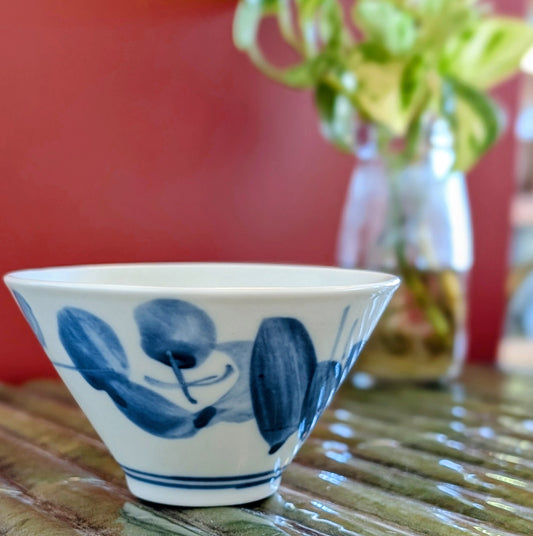 White porcelain tea cup painted with blue leaf design on a green mat against a terracotta background.
