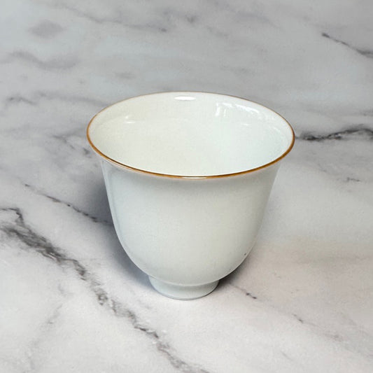White ceramic cup with gold rim on a marble surface