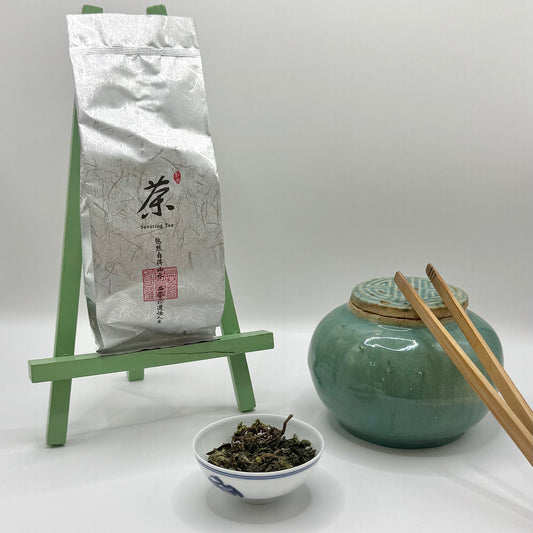 Tea packaging, green ceramic jar, bowl of tea leaves, and chopsticks on a white background