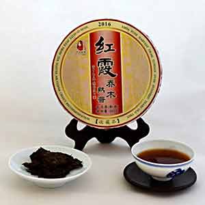 Tea cake with a red label on a stand, accompanied by a cup of tea and a bowl of tea leaves.