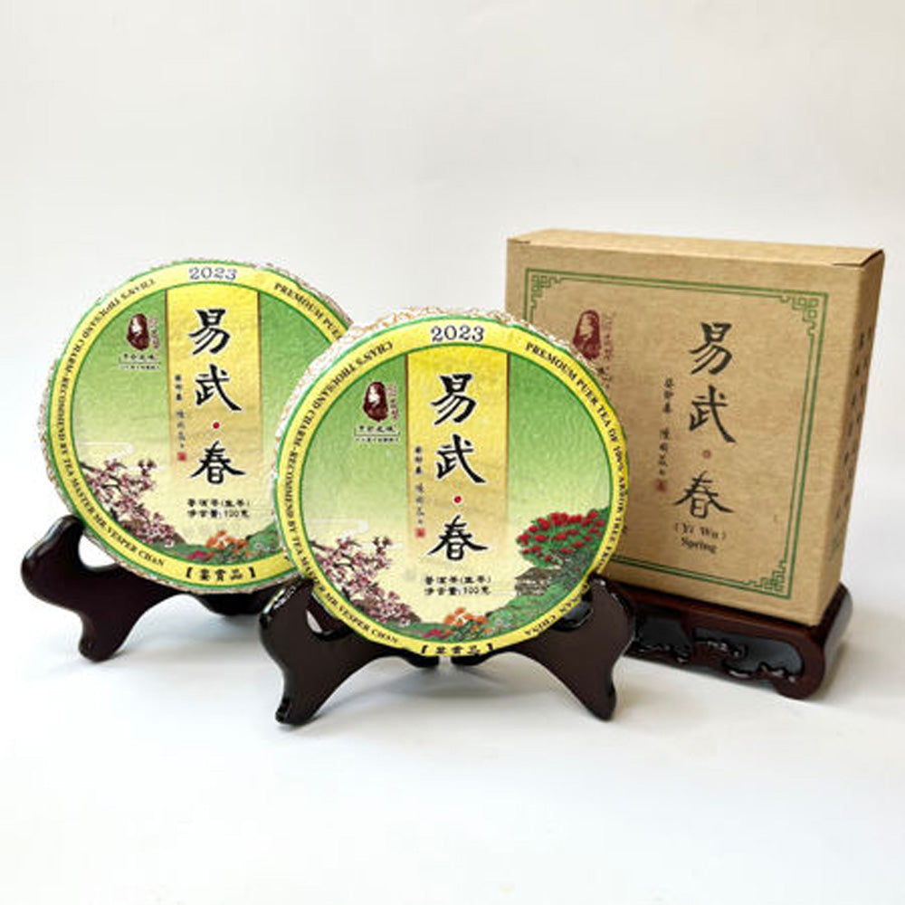 Two green tea packages with yellow labels and a cardboard box on a white background