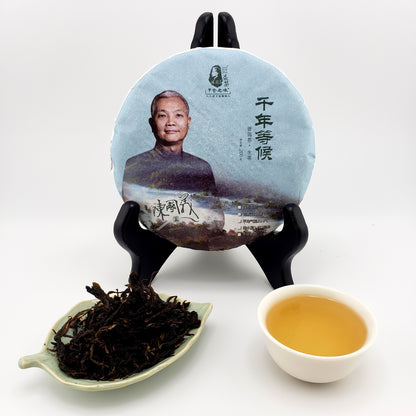Tea cake on a stand with a plate of dried tea leaves and a cup of brewed tea
