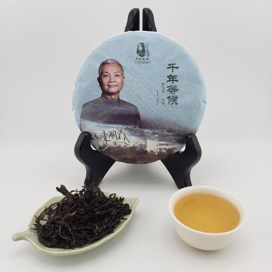Tea cake on a stand with a plate of dried tea leaves and a cup of brewed tea