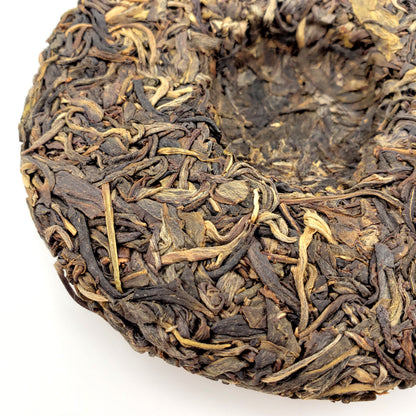 Close-up of a compressed tea cake with dried tea leaves on a white background