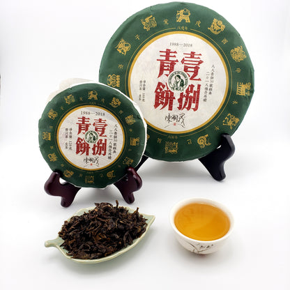 Two green tea cakes with red text on a white background, accompanied by a small bowl of tea and a scoop of tea leaves.