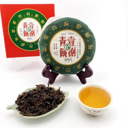 Green tea cake with a red box, a cup of tea, and a bowl of tea leaves on a white background
