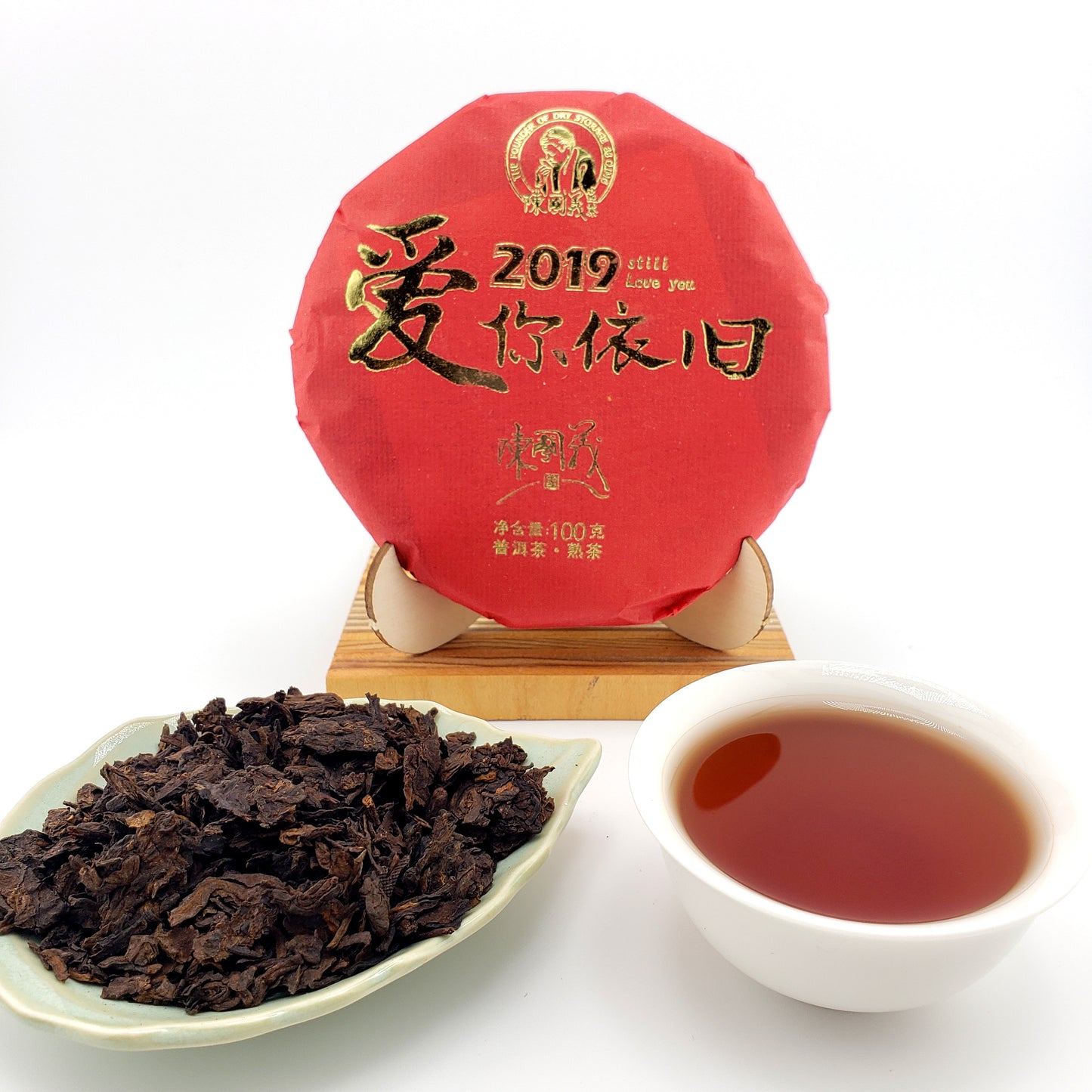 Red tea cake with gold text, a white cup of tea, and a scoop of tea leaves on a white background.