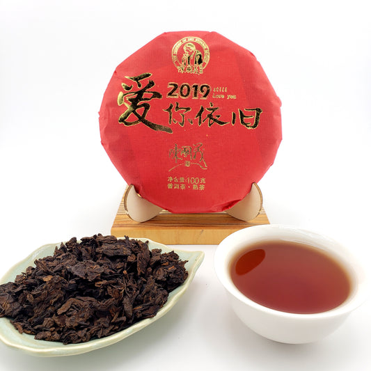 Red tea cake with gold text, a white cup of tea, and a scoop of tea leaves on a white background.