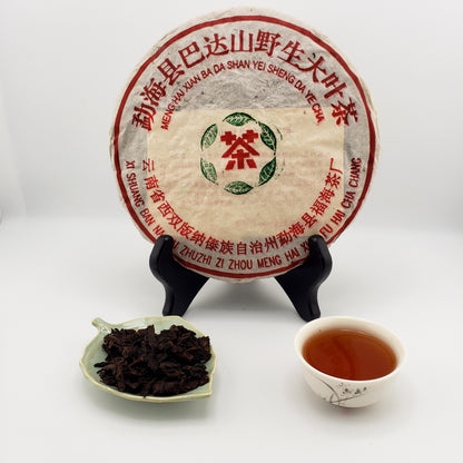 Bada Mountain pu-erh tea cake with a tray of tea leaves and a cup of brewed tea