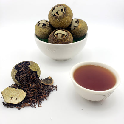 Green mandarins stuffed with tea leaves in a white container with a cup of tea on a white background