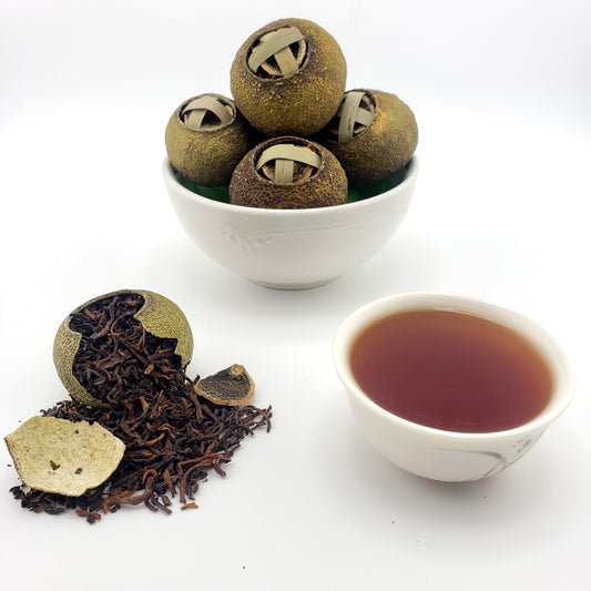 Green mandarins stuffed with tea leaves in a white container with a cup of tea on a white background