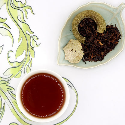 Tea leaves on a small plate with a cup of tea on a decorative tablecloth.