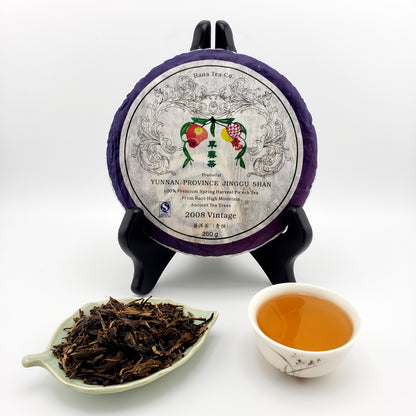 Tea cake of pressed Pu-erh tea with decorative wrapper, plate of dry tea leaves, and cup of brewed tea.