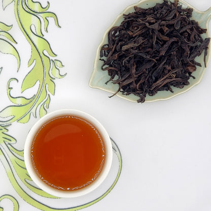 Dried oolong tea leaves on a leaf-shaped plate with a cup of brewed tea on a decorative white and green background.