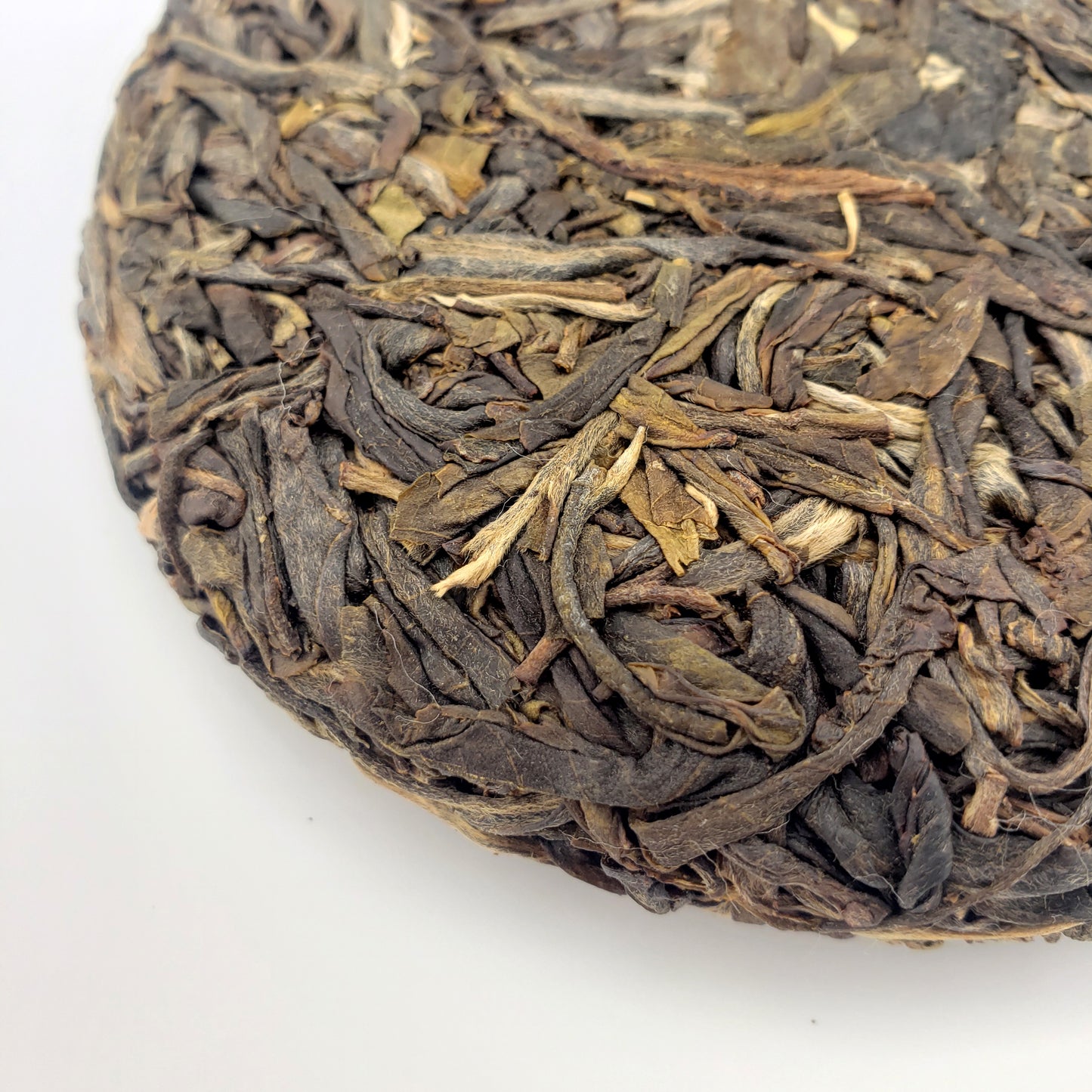 Close-up of a compressed tea cake with dried tea leaves on a white background