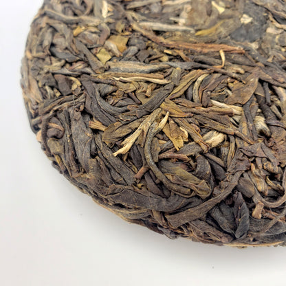 Close-up of a compressed tea cake with dried tea leaves on a white background