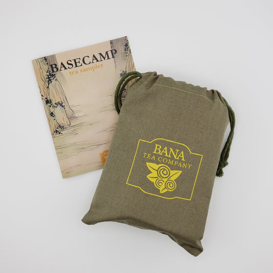 An olive green drawstring pouch with a yellow 'BANA TEA COMPANY' logo, shown next to a printed insert card labeled 'BASECAMP tea sampler' on a light gray background.