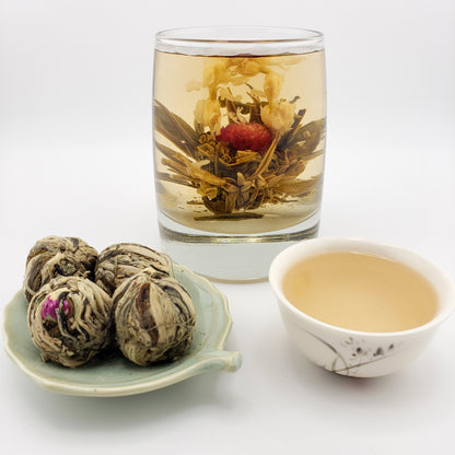 Blooming tea bulbs, cup of brewed tea, and glass showing the tea blooming, with red and white flowers.