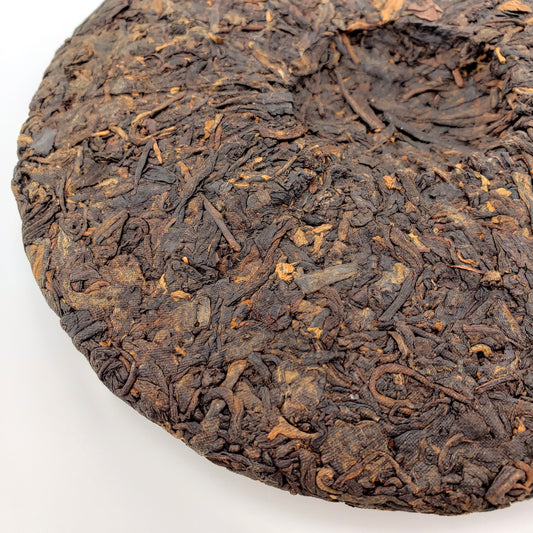 Close-up of a round, pressed tea cake with dark brown tea leaves on a white background