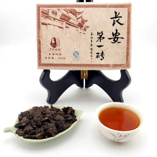 Tea brick with decorative wrapper, plate of tea leaves broken from the brick, and a cup of brewed tea.