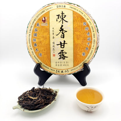 Round tea cake with a yellow label next to a cup of tea and a tea leaf sample on a white background