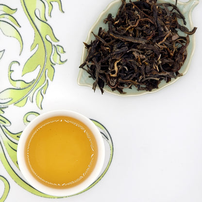 Dried tea leaves on a leaf-shaped plate with a cup of brewed tea on a decorative white background.