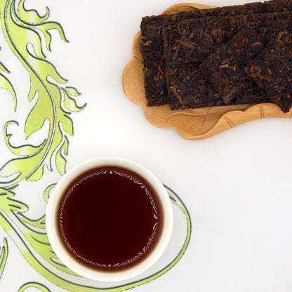 Puer tea bricks on a wooden board with a cup of tea on a decorative white and green plate.