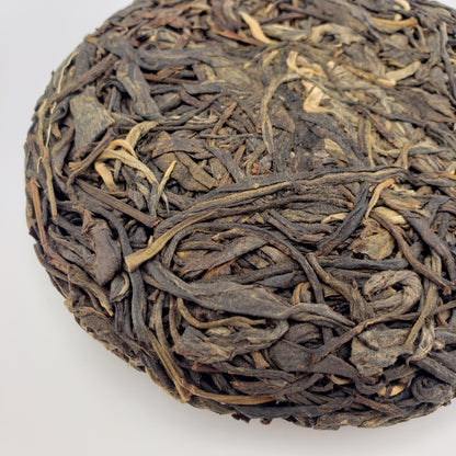 Close-up of a compressed tea cake with twisted tea leaves on a white background