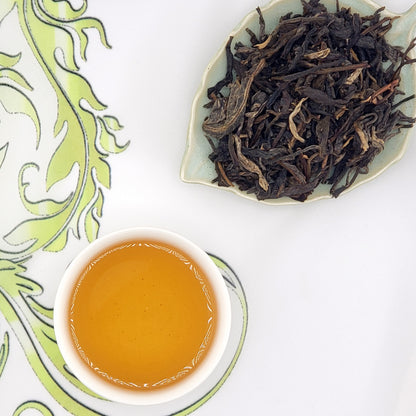 Tea cup with brewed tea and a dish of dry tea leaves on a decorative white and green background.