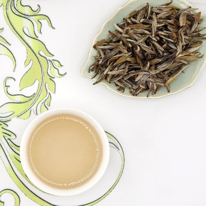 Tea leaves on a plate with a cup of brewed tea on a decorative mat