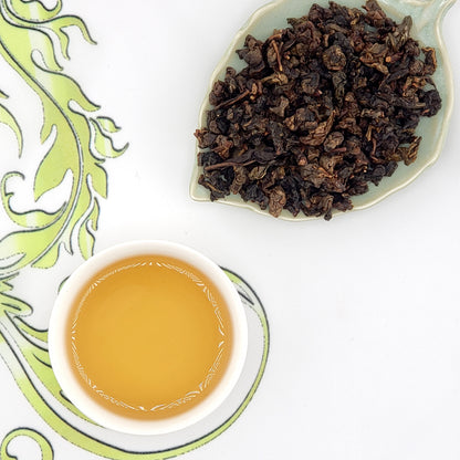 Dry tea leaves on a leaf-shaped plate with a cup of brewed tea on a decorative white background.